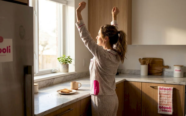 Une femme s'étire doucement dans sa cuisine baignée de soleil, profitant des premiers rayons du matin.